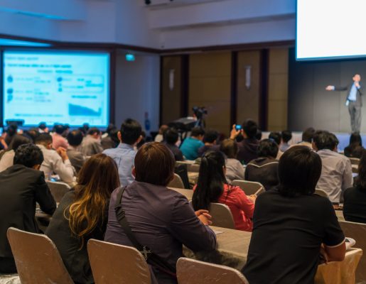 Rear side of Audiences sitting and listening the speackers on the stage in low light conference hall, event and seminar concept